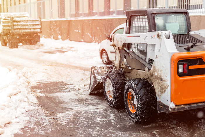 Small tractor loader machine clean  and load snow and ice into a truck from a city streets after heavy snowfall